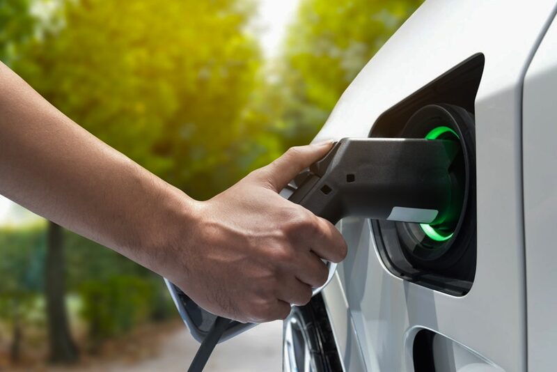 A hand plugging a charging cable into the charging port of a white electric car