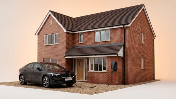 A black electric car charging from a wall-mounted EV charger outside a brick detached house