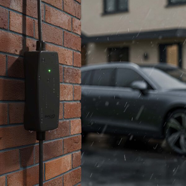 A Sync Energy portable Mode 2 EV charger mounted on a brick wall in the rain with an electric car parked in the background
