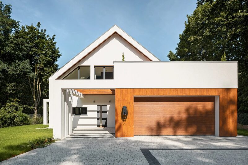 A wall-mounted EV charge point installed beside the garage door of a modern white and timber-clad house