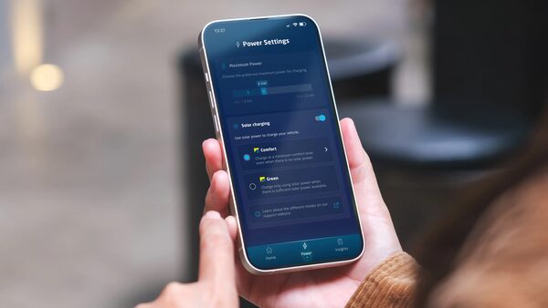 A hand holding a smartphone showing an EV charging app's Power Settings screen with solar charging options