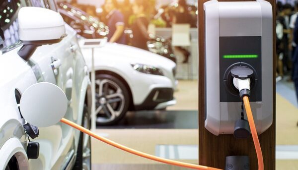 An electric car charging from a wall-mounted EV charge point with an orange cable at what appears to be a showroom or exhibition