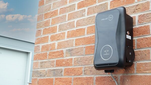 A black Project EV wall-mounted electric car charge point installed on a red brick house wall
