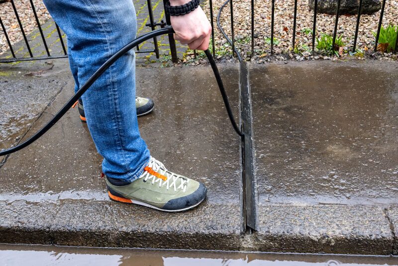 A person running a black EV charging cable through a cable protector channel across a wet pavement