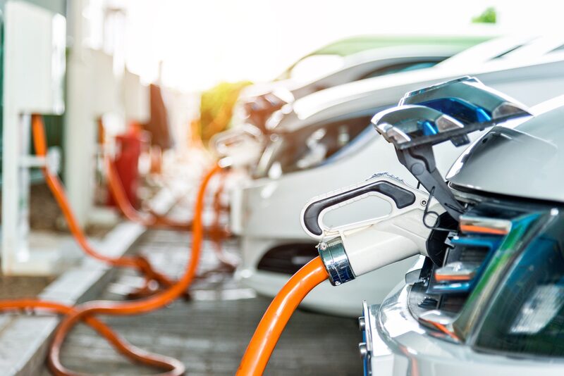 Electric cars charging at a public charging station with orange cables plugged into their charge ports