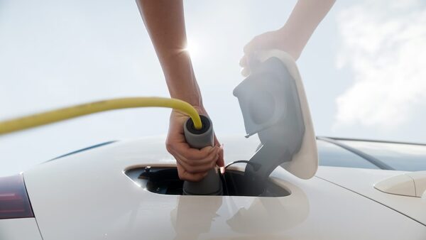 A person plugging a yellow charging cable into the charging port of a white electric car