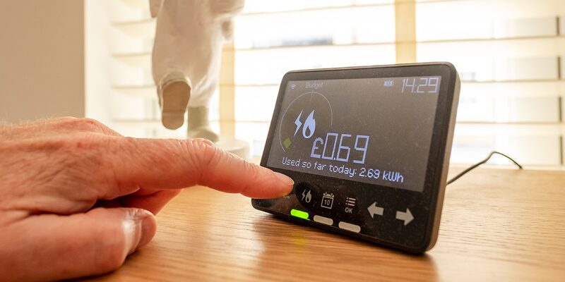 A finger pressing a smart meter in-home display showing today's energy use of 2.69 kWh costing £0.69