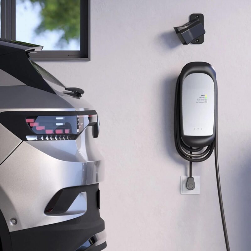 A wall-mounted GivEnergy EV charger with coiled cable next to a parked electric car outside a house