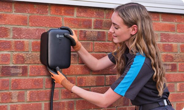 A technician in gloves installing a black Hive EV charger on a red brick wall outside a house