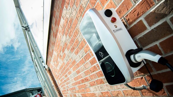 A white wall-mounted EV charge point with a tethered cable installed on a red brick wall