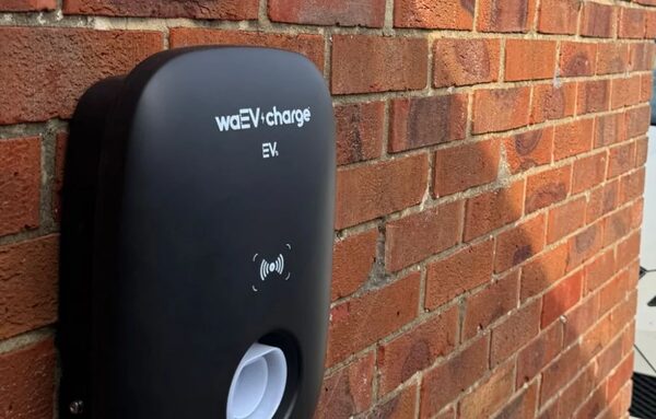A black waEV-charge EV home charger mounted on a red brick wall