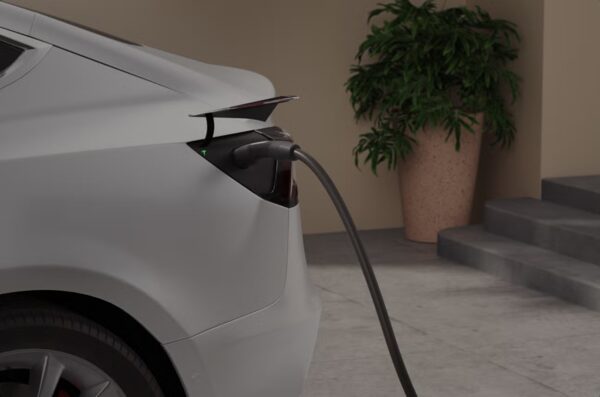 A white electric car being charged with a cable plugged into its charge port outside a house
