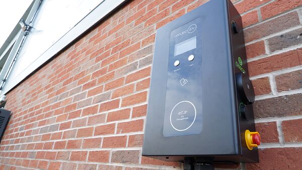 A black Project EV wall-mounted electric car chargepoint installed on a red brick wall