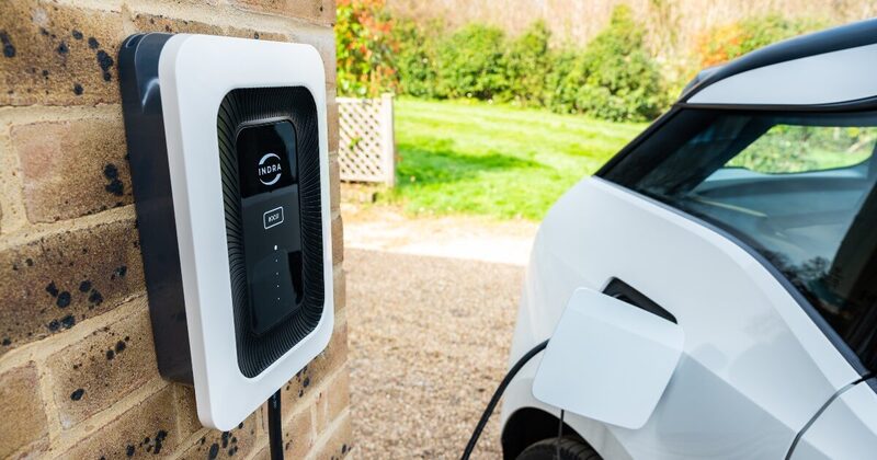An Indra Smart LUX wall-mounted EV charger on a brick wall charging a white car