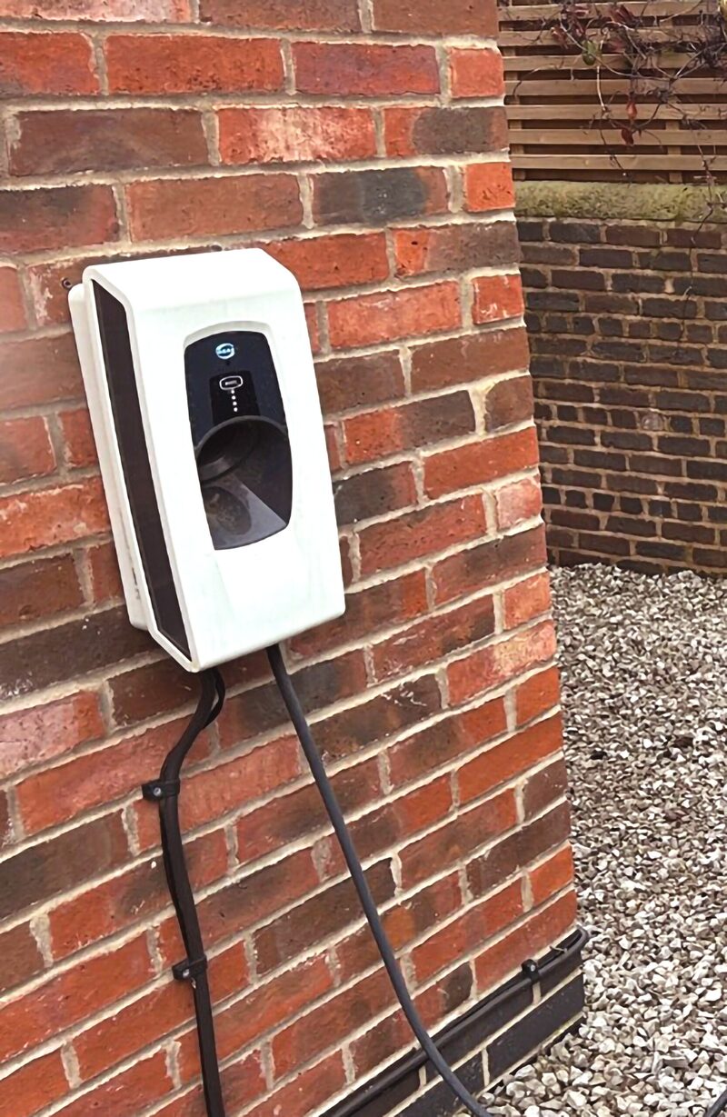 A white Indra Smart PRO EV charger mounted on a red brick house wall with its cable hanging down