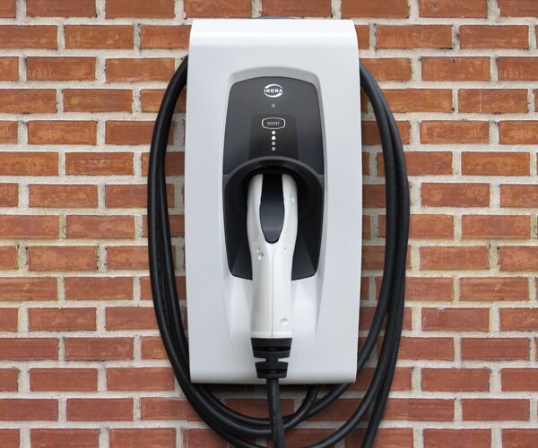 An Indra wall-mounted electric vehicle charge point with coiled cable and plugged-in connector on a red brick wall
