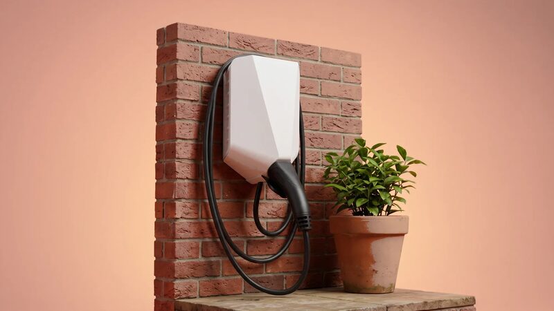 A white wall-mounted EV charge point with coiled cable on a brick wall next to a potted plant
