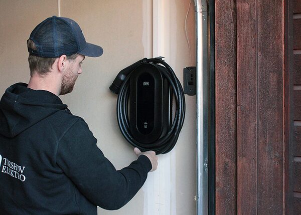 An electrician installing a black DEFA wall-mounted EV charge point with coiled cable on a garage wall