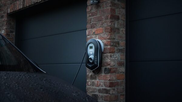 A black zappi EV charge point mounted on a brick pillar beside a dark garage door, with a car parked nearby