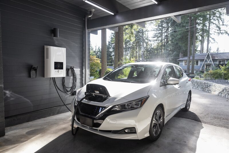 A white Nissan Leaf charging from a wall-mounted home EV charger in a garage