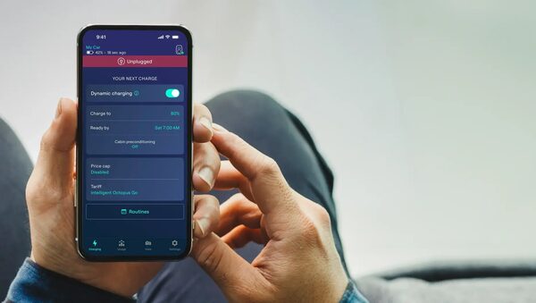 A person holding a smartphone showing the Ohme EV charging app with Intelligent Octopus Go tariff settings