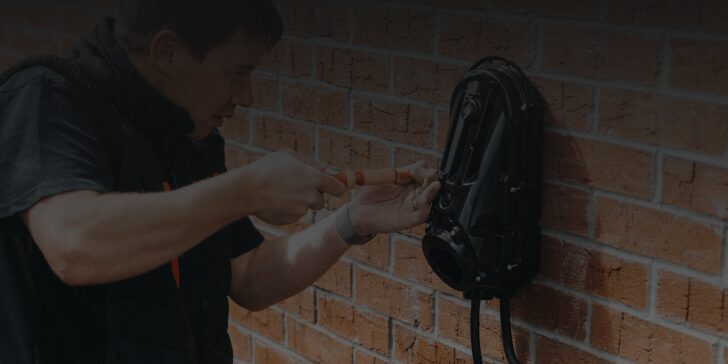 A technician installing a black myenergi EV charge point on a brick wall