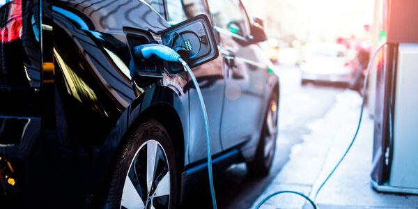 A black electric car plugged in with a charging cable at a public charge point on a street