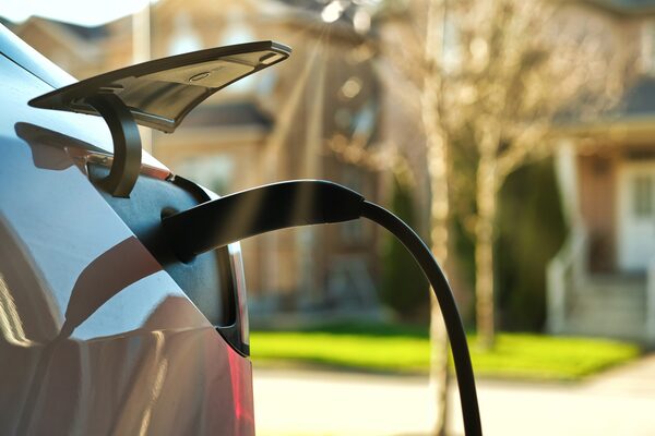 A charging cable plugged into the open charge port of an electric car parked on a suburban street