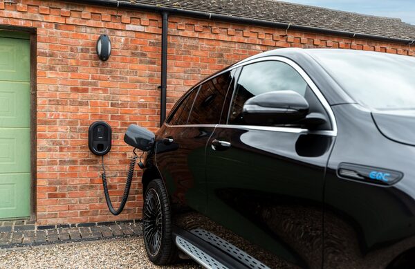 A black wall-mounted Ratio EV home charger on a brick garage wall charging a black electric SUV