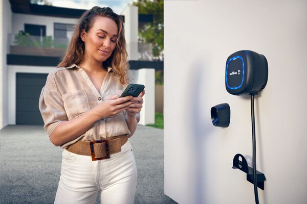 A woman using her phone next to a black Wallbox EV charger mounted on an outdoor wall