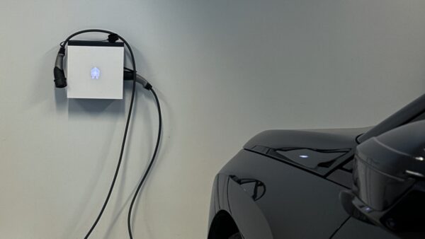 A wall-mounted EV charging point with cable next to a parked black electric car