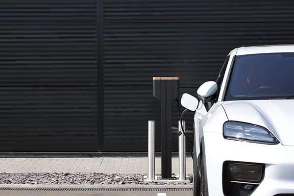 A white electric car plugged into a black wall-mounted EV charge point outside a dark building