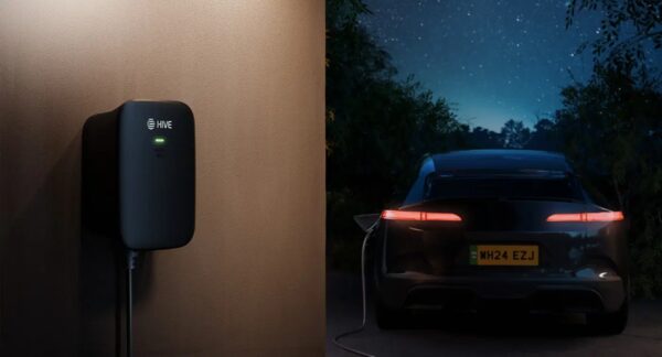 A black Hive EV charger mounted on a wall next to an electric car charging at night