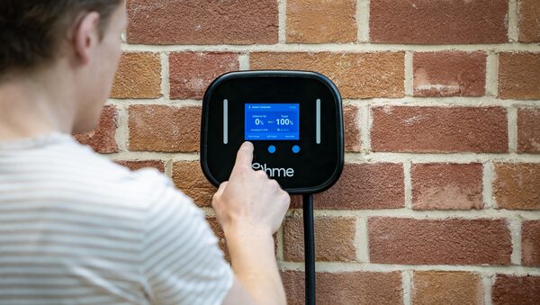 A man pressing the screen of an Ohme Home Pro EV charger mounted on a brick wall