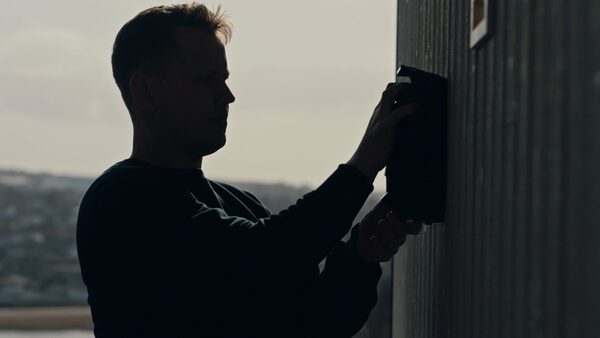 A man installing a black Easee EV charger on an exterior wall