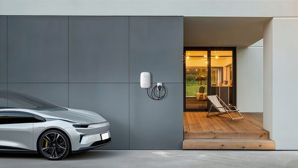 A white Sungrow wall-mounted EV charger with coiled cable on a grey modern house wall beside a parked silver car