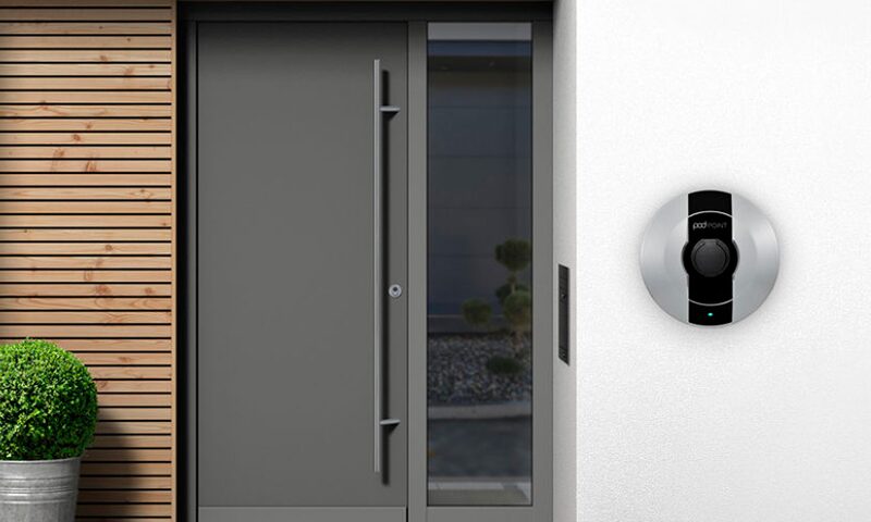 A Pod Point electric car charger mounted on a white wall beside a grey front door of a house