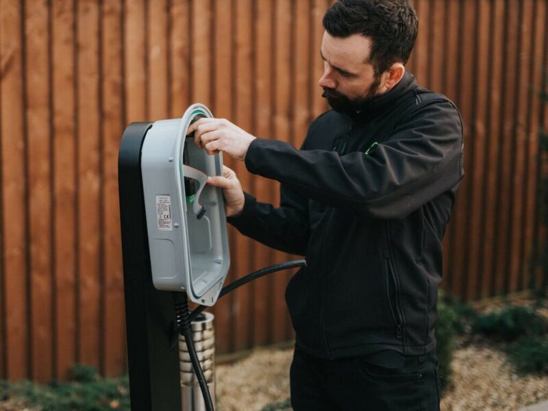 A technician installing a myenergi Zappi EV charger on a post outdoors in front of a wooden fence