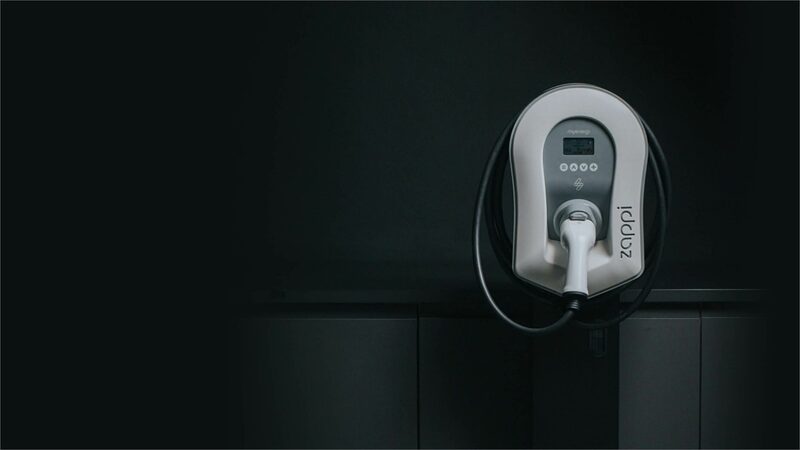 A myenergi zappi EV charge point mounted on a dark wall with its tethered cable holstered