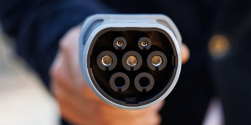 A close-up of a Type 2 EV charging plug held out towards the camera