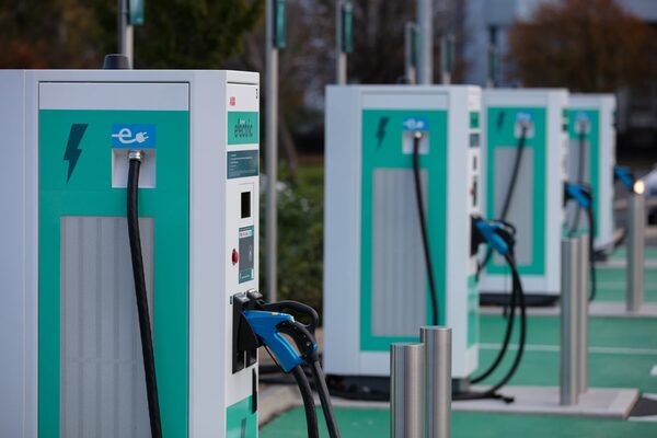 A row of green and white public electric vehicle rapid chargepoints with blue cables at a charging hub