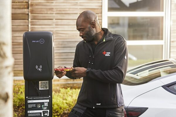 An electrician in a NICEIC-branded jacket working on an Andersen EV charge point outside a house next to a parked car