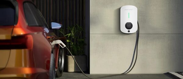 A red car charging from a white wall-mounted EV charger outside a house