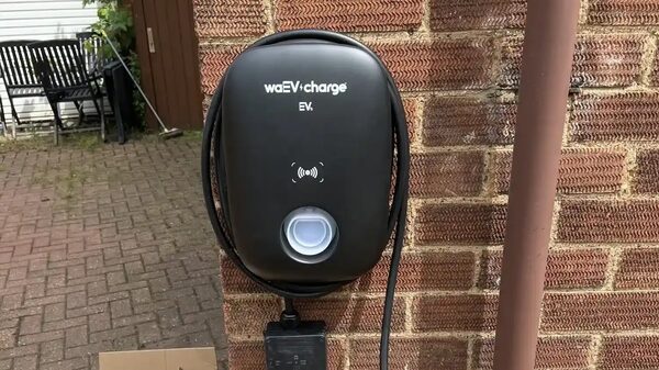 A black waEV-charge EV home charger mounted on a brick house wall with coiled cable