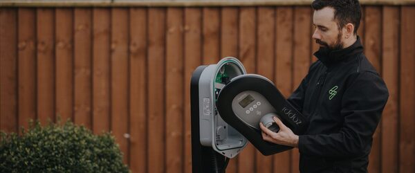 An installer in a black myenergi jacket fitting the front cover onto a zappi EV charge point outdoors