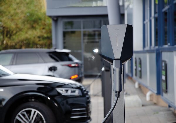 A wall-mounted EO electric vehicle charge point with tethered cable at a car park, with cars charging in the background