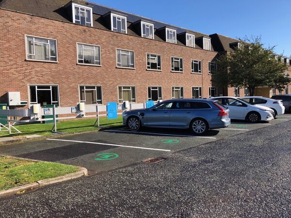 Electric cars charging at wall-mounted charge points in a car park outside a brick office building