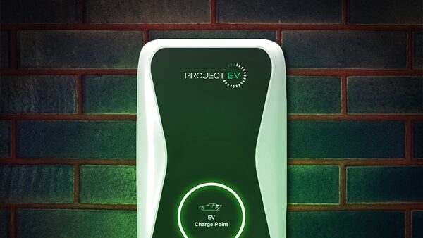 A green and white Project EV wall-mounted electric car charge point on a brick wall