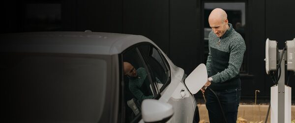 A man plugging a charging cable into a grey electric car next to a wall-mounted EV charger