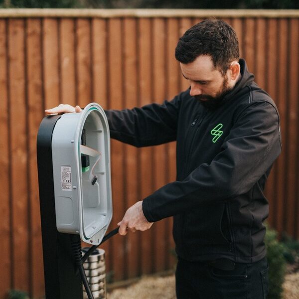 A technician in a black myenergi jacket installing a zappi EV charge point on a post in front of a wooden fence